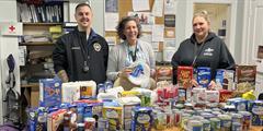 Three people stand behind a table of donated food.