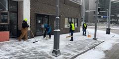 Four people shoveling snow on a city sidewalk.