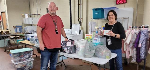 Two people stand by a table with bags full of donated supplies on it.