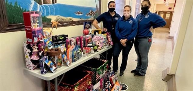 Three people stand with a table full of toy donations
