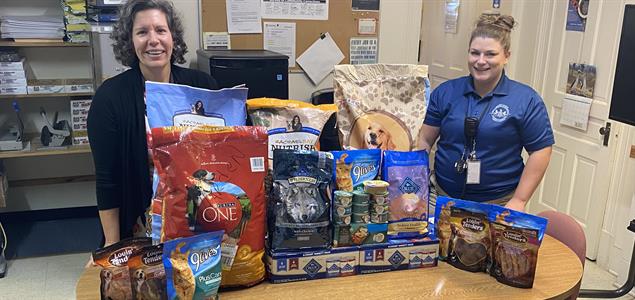 Two people stand with a table full of donated pet food