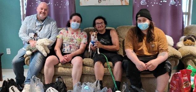 Four people and a dog sit on a couch behind donated items
