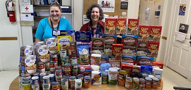 Two people stand behind a table of donated food