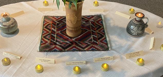 A table with candles and names of imams circling a vase of flowers in the middle