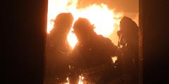 Three firefighters are silhoutted in front of a fire inside a building