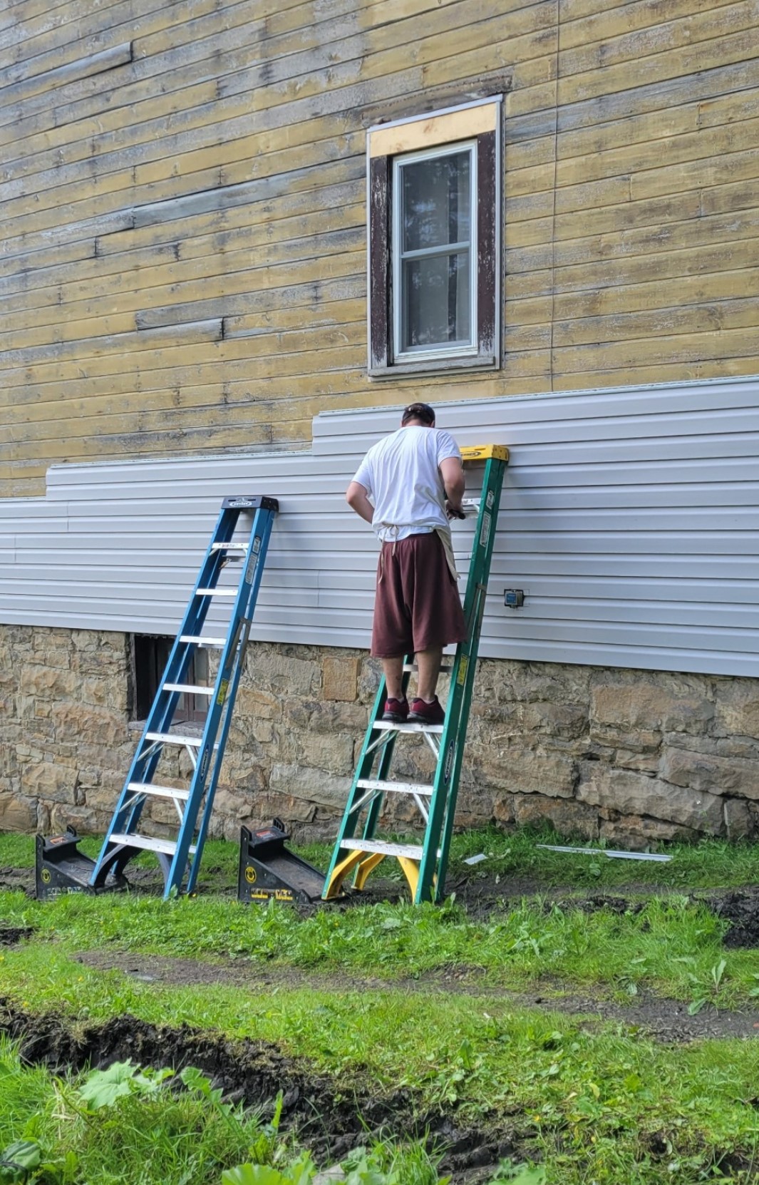 A person on a ladder puts siding on a house