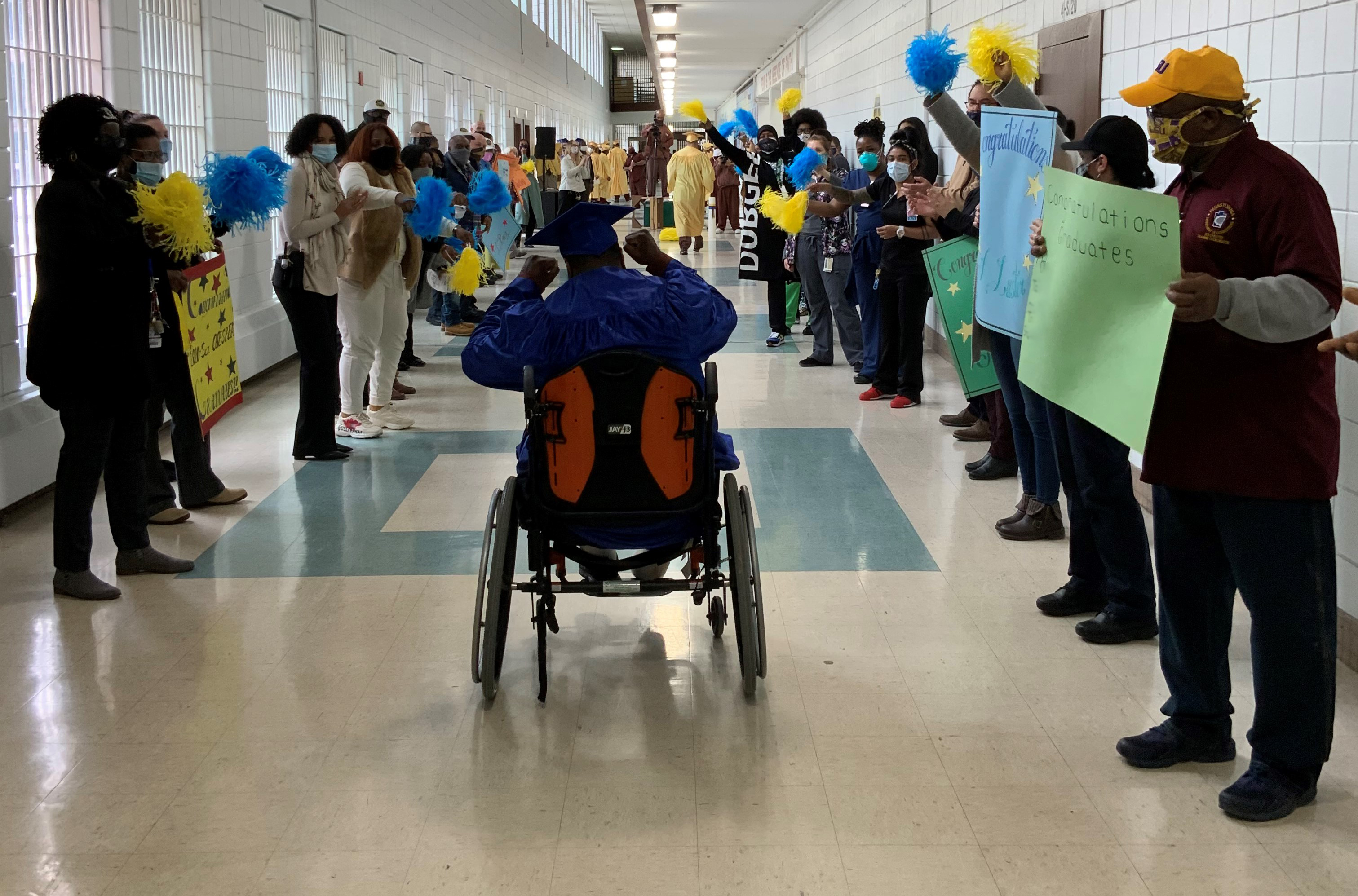 An inmate graduate goes down SCI Chester's main hallway with people cheering him on