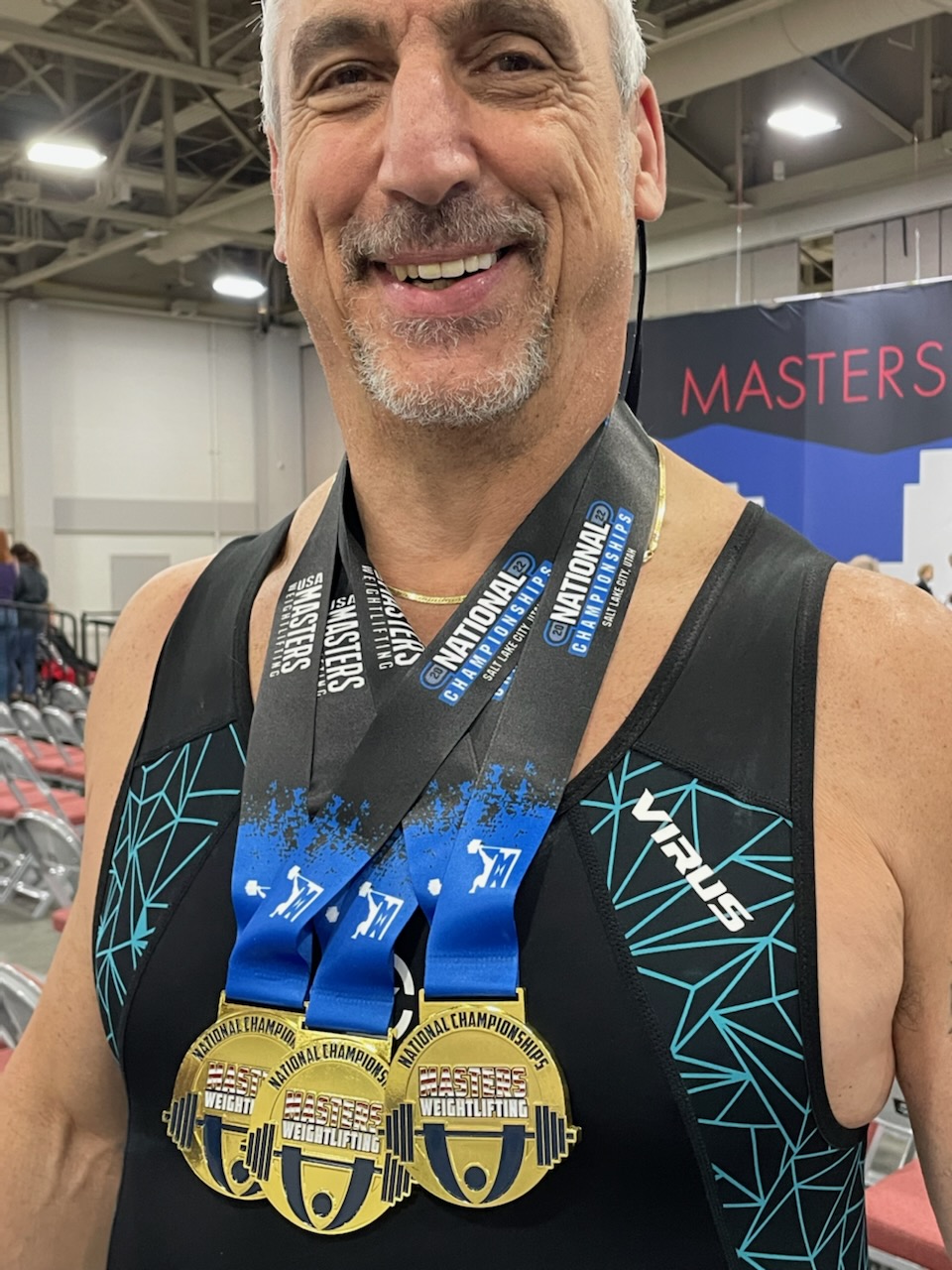 A man smiles with three gold medals around his neck