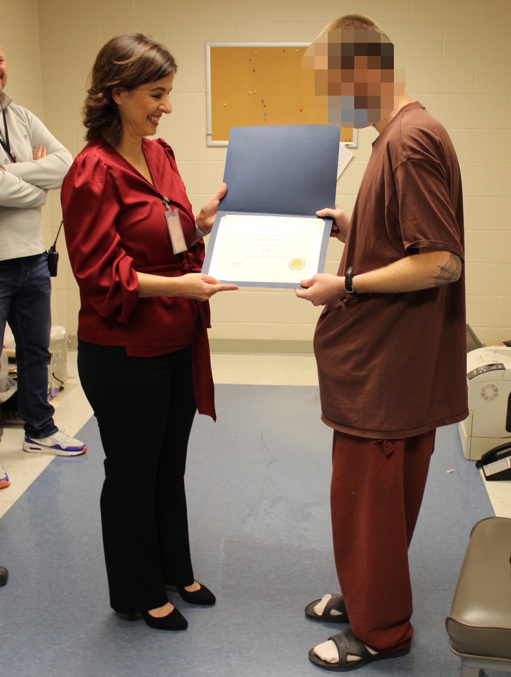 An inmate and his teacher stand holding his diploma