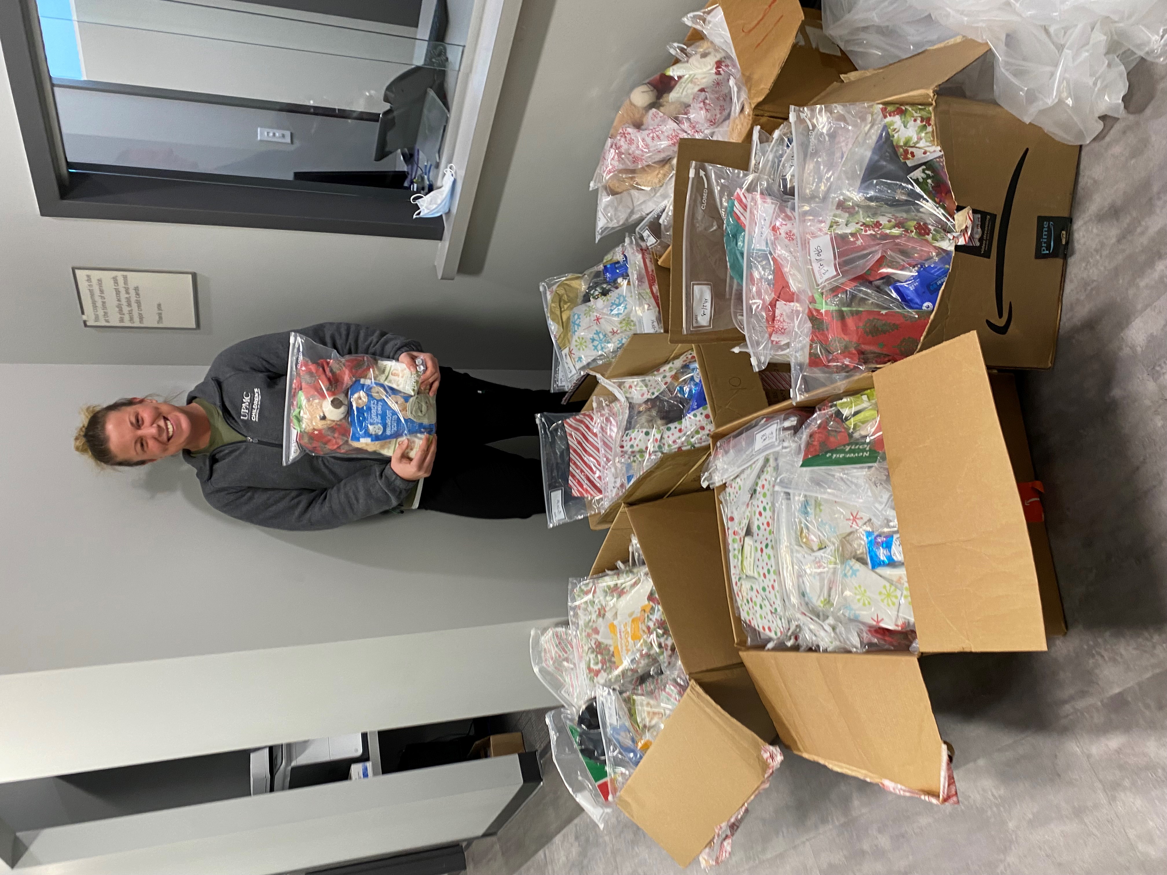 A Children's Hospital of Pittsburgh employee holds a care package in front of boxes of care packages purchased and put together 