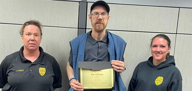 Three people stand with one in the middle holding a certificate