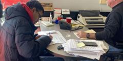 A man signs paperwork on a desk at a car dealership.