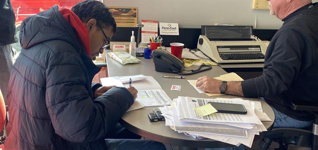 A man signs paperwork on a desk at a car dealership.