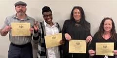 Four people stnading in a row holding certificates