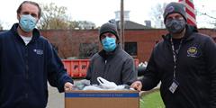 Three men stand with a box of donations