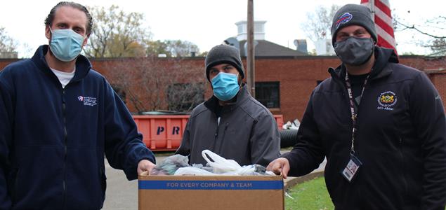 Three men stand with a box of donations