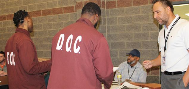 Two incarcerated individuals speak with an attendee at the SCI Albion Reentry Career Fair