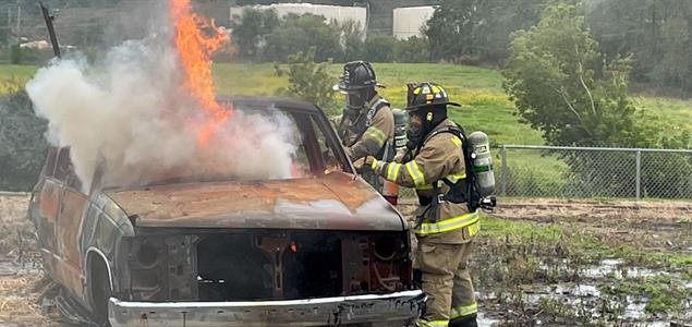 Two firefighters put out a burning car