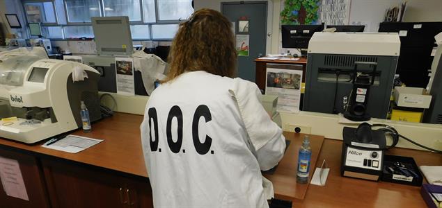 A woman in a DOC lab coat works on a lab table