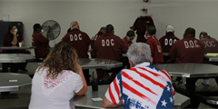 Two Camp Hill employees and a group of inmates watch an inmate speak to the group