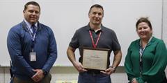 Psychological Service Specialist Thaddeus Gross stands between two people while he holds a certificate.