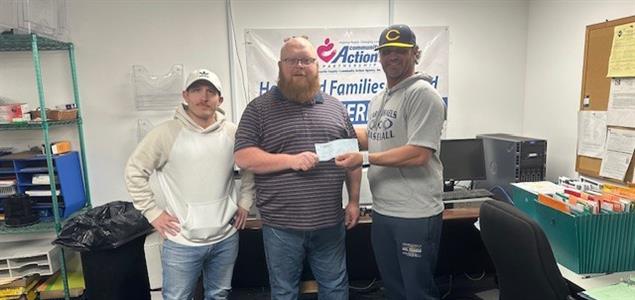 Three people standing in an office with two holding a check.