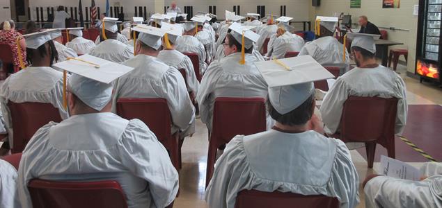 Incarcerated graduates wearing white caps and gowns at SCI Forest sit during their graduation ceremony