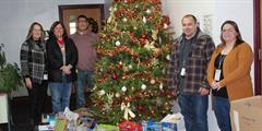 Five people around a Christmas tree with donated presents under it