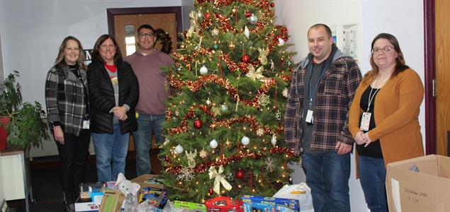 Five people around a Christmas tree with donated presents under it