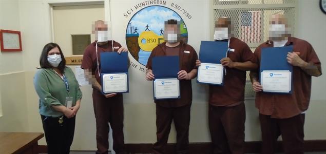 Four graduates stand with their teacher and show off their certificates