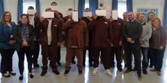 A group of inmates holding certificates of completion over their faces standing with DOC and Penn State staff