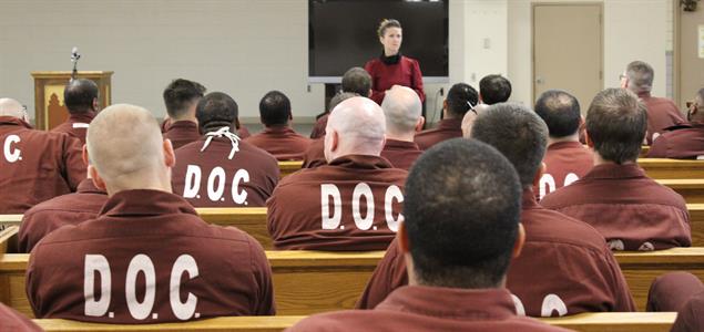 A woman speaks to an audience of inmates