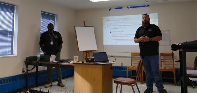 Two men stand at the front of a room giving a presentation