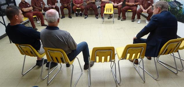 Three people sitting across from a group of inmates