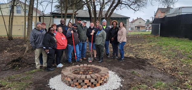 A group of SCI Mercer volunteers stand around a fire pit they helped build