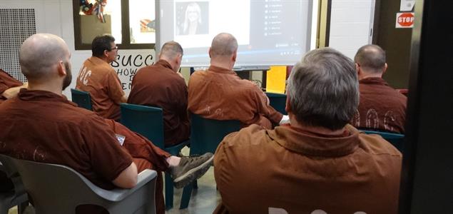 A group of inmates watch a presentation on a screen