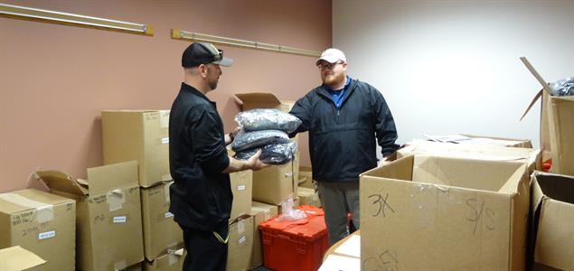 A man gives a bundle of uniforms to another man