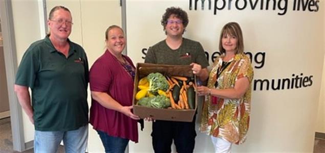 Four people holding a box of vegetables