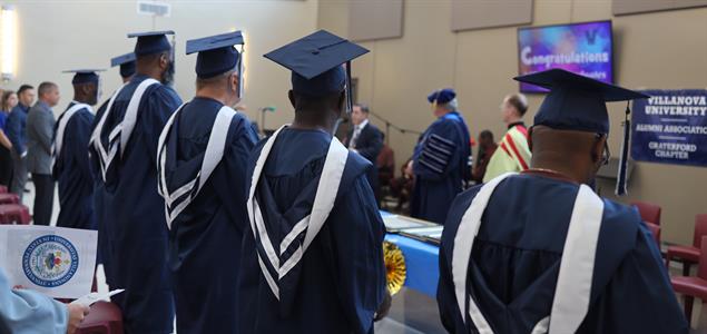 Graduates stand watching a speaker at a graduation ceremony