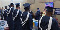 Graduates stand watching a speaker at a graduation ceremony