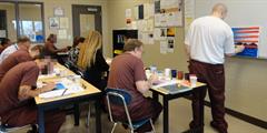 An incarcerated individual shows a class of inmates and employees how to paint a picture.