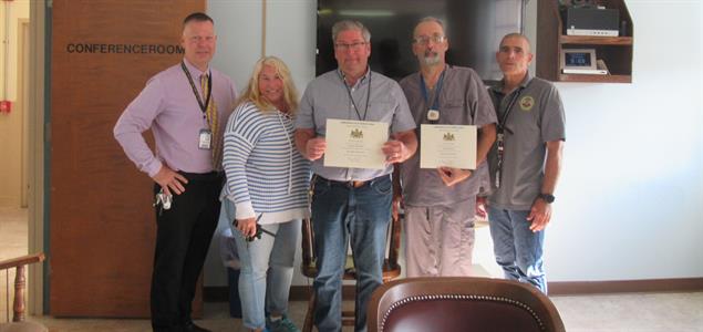Five people standing in a line with two holding certificates