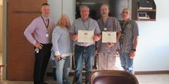 Five people standing in a line with two holding certificates