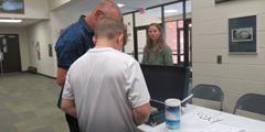 A student gets fingerprinted by an adult while another adult observes