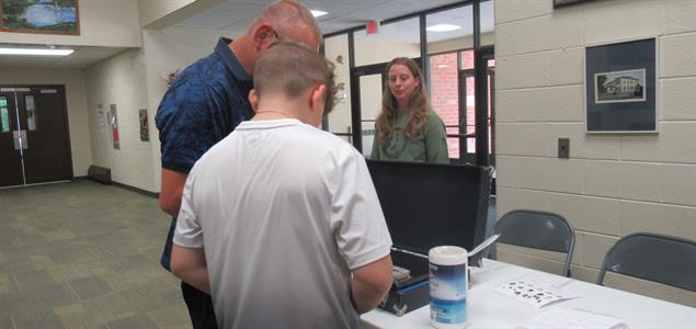 A student gets fingerprinted by an adult while another adult observes