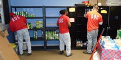 Three incarcerated individuals stack food on shelves.