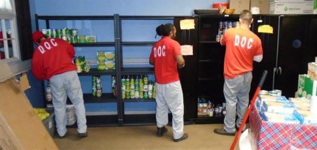 Three incarcerated individuals stack food on shelves.