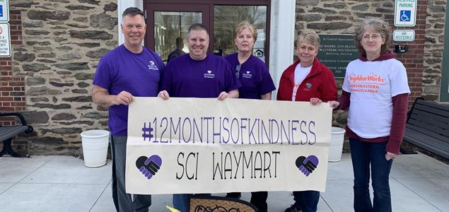 Five people standing outside holding a banner that says "#12MonthsOfKindness SCI Waymart"