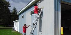 Two inmates paint a building.