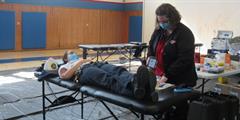 A person lays down donating blood with a nurse standing beside